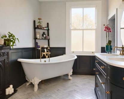 an esnuite bathroom with roll top bath, dark wall panelling, marble tile floor, double basin and reclaimed fireplace